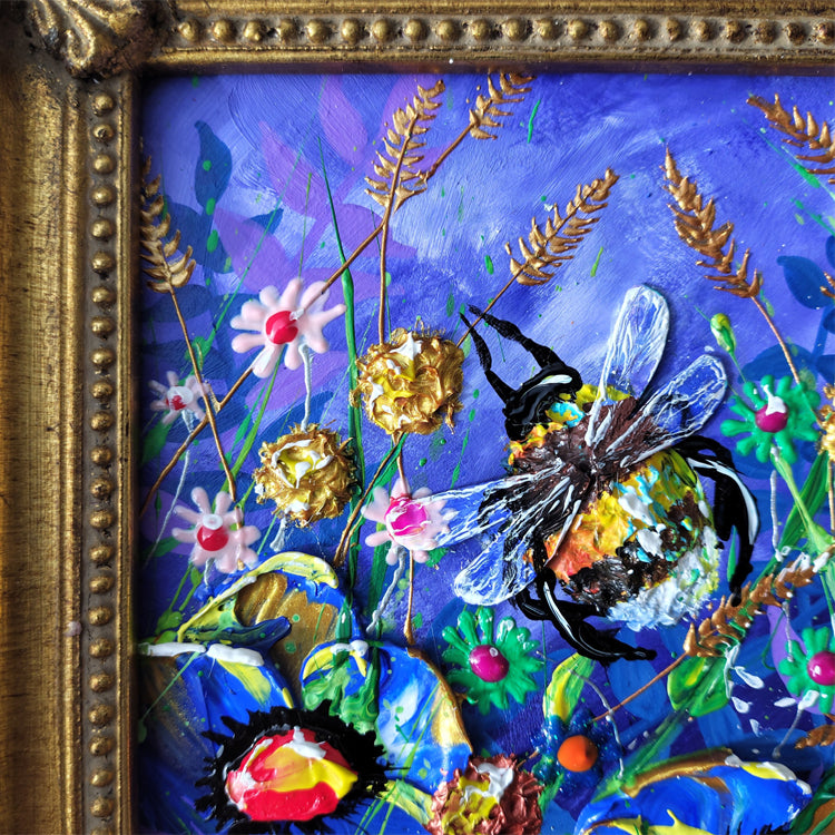 A close-up of a colorful mixed-media painting featuring a bee among flowers, enclosed in an ornate gold-toned frame. The artwork has a dominant blue-purple background with gold grasses, white and pink flowers, green leaves, and a multicolored bee.