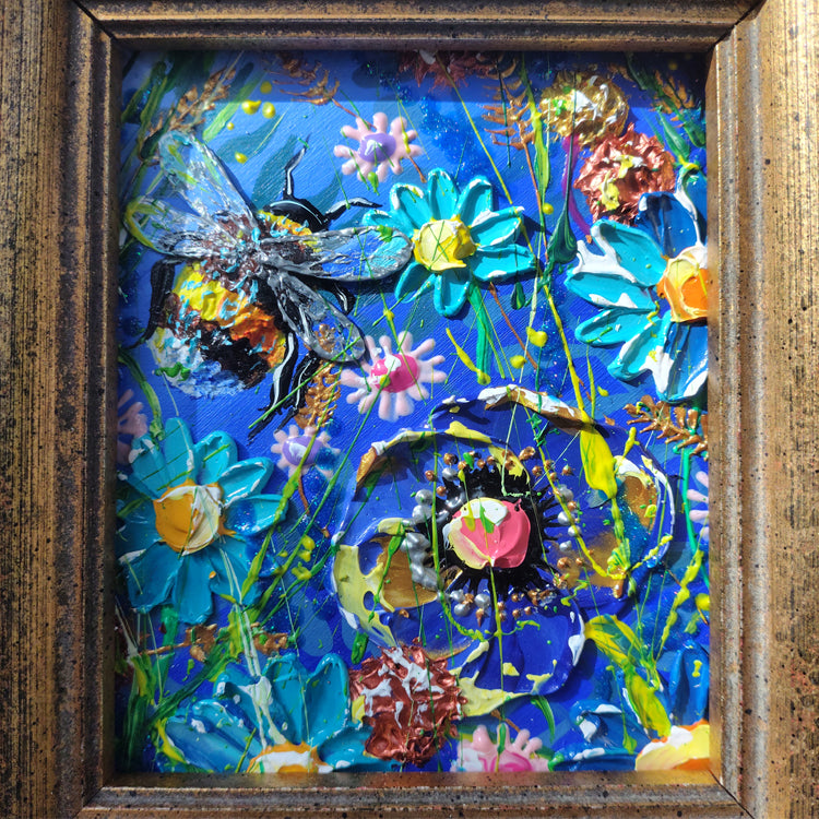 A framed square art piece featuring a colorful abstract floral and insect scene on a vivid blue background, surrounded by a textured brown wooden frame.