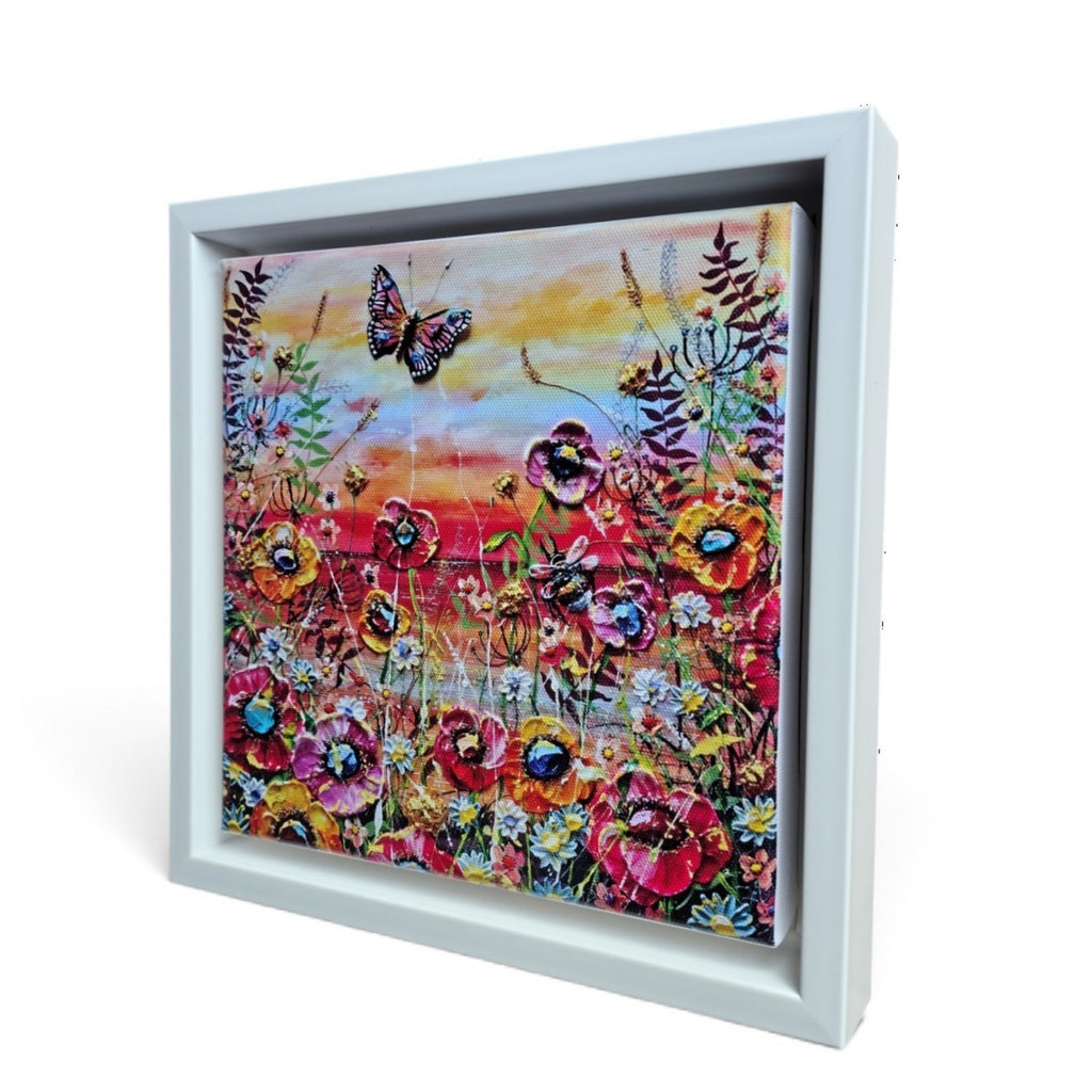 A square framed floral artwork limited edition print shown at an angle against a white background. The painting depicts colorful flowers with a butterfly and a warm sunset sky, set in a white shadowbox-style frame.