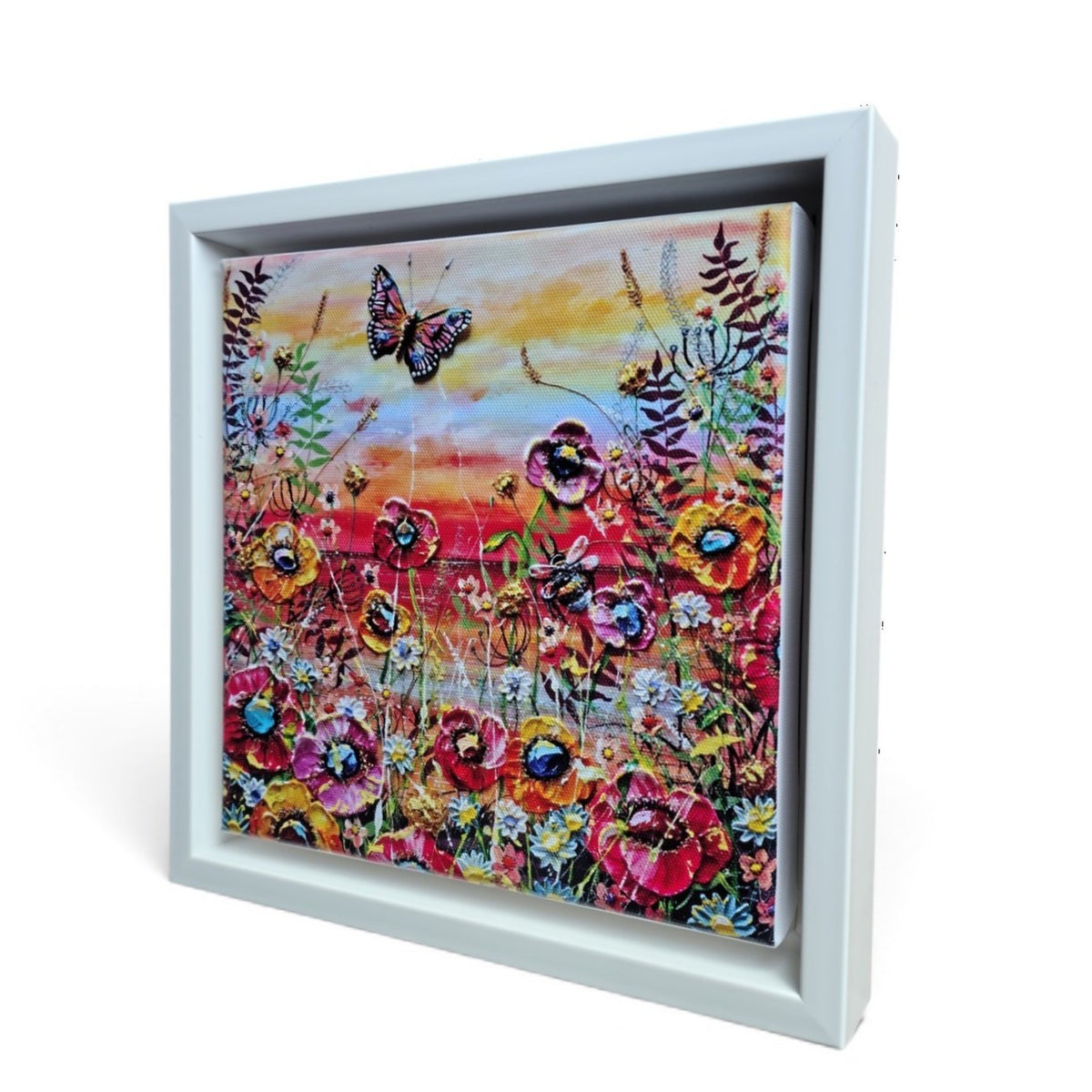 A square framed floral artwork limited edition print shown at an angle against a white background. The painting depicts colorful flowers with a butterfly and a warm sunset sky, set in a white shadowbox-style frame.