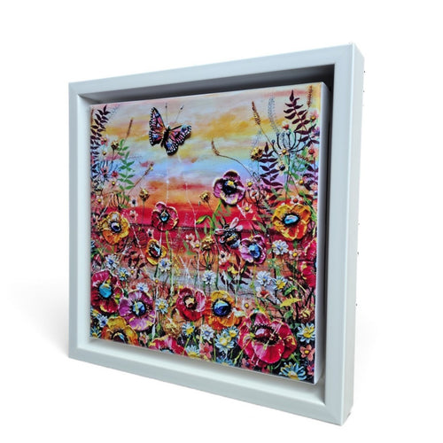 A square framed floral artwork limited edition print shown at an angle against a white background. The painting depicts colorful flowers with a butterfly and a warm sunset sky, set in a white shadowbox-style frame.