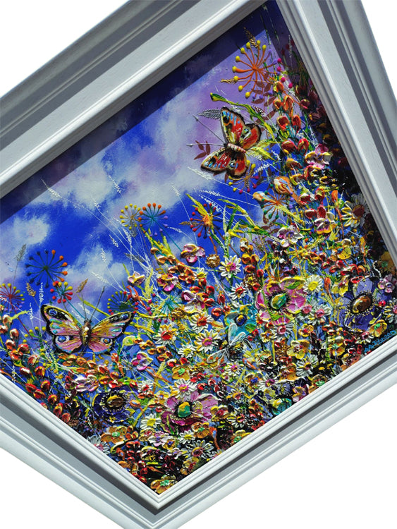 A framed colorful painting depicting a vibrant field of flowers and butterflies under a blue sky, shown at an angle with a white frame.