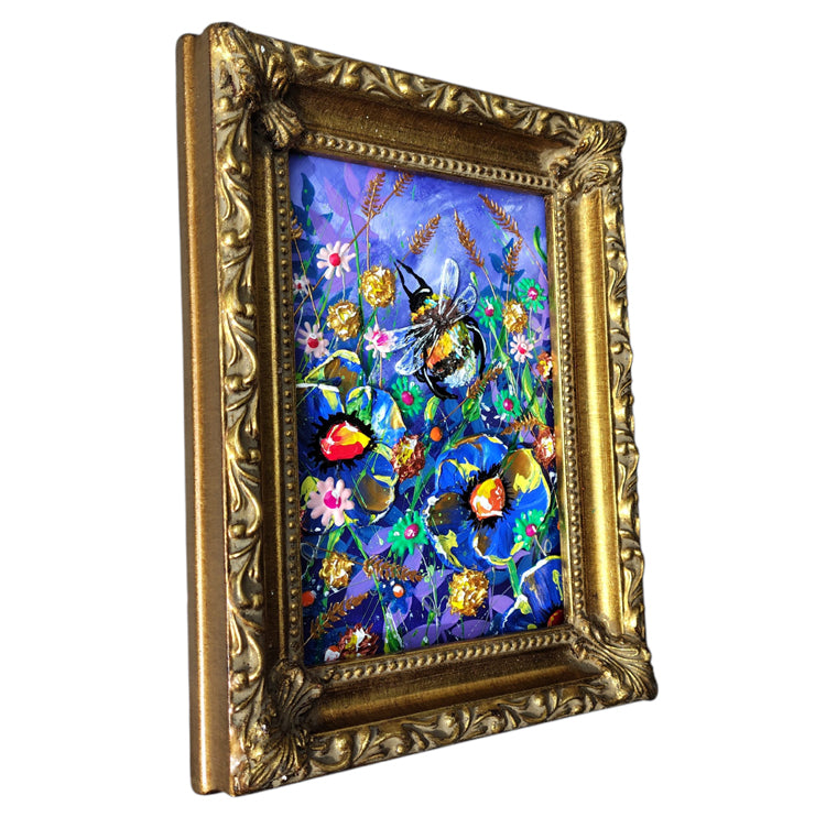 An ornate gold, baroque style picture frame containing a colorful painting of a bee among flowers, shown on a plain white background.