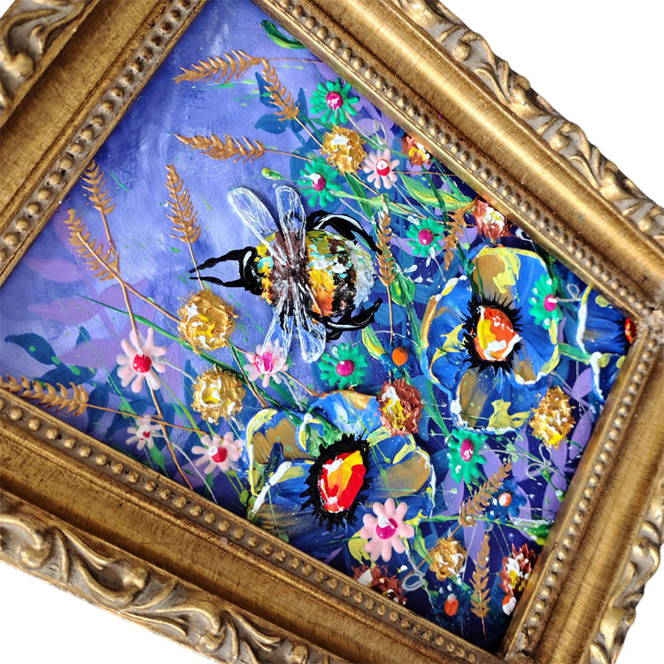 A framed painting featuring a bumblebee among blue flowers and green foliage on a purple background, set in an ornate gold frame.