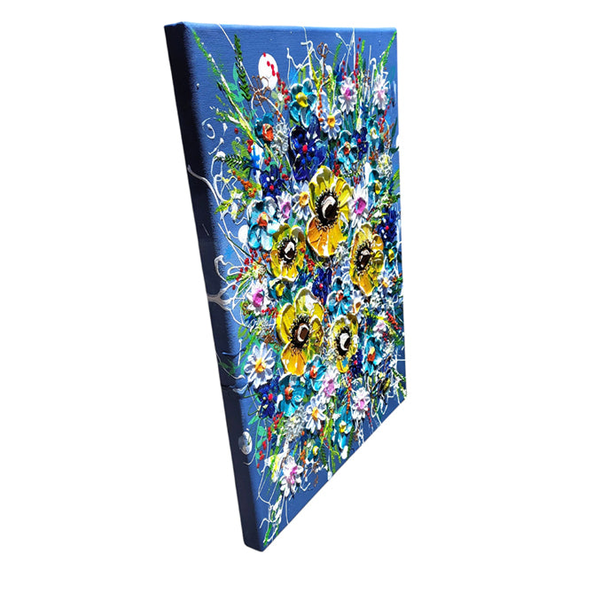 A square canvas painting shown at an angle, featuring a vibrant floral bouquet with yellow, blue, white, and pink flowers on a deep blue background.